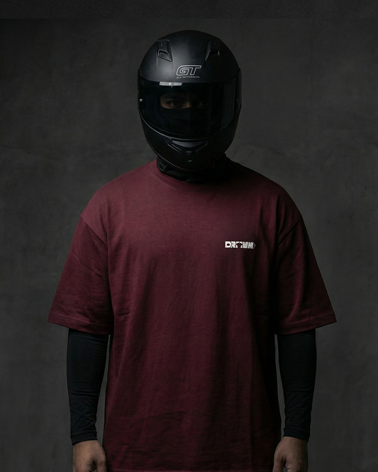 Person wearing a maroon t-shirt with drivn logo and a black helmet on a dark background