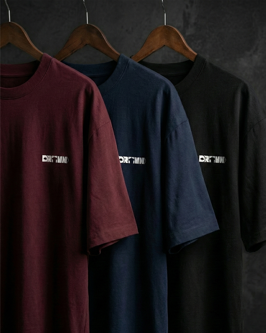 Three t-shirts in maroon, navy, and black with drivn logo hanging on wooden hangers against a dark background.