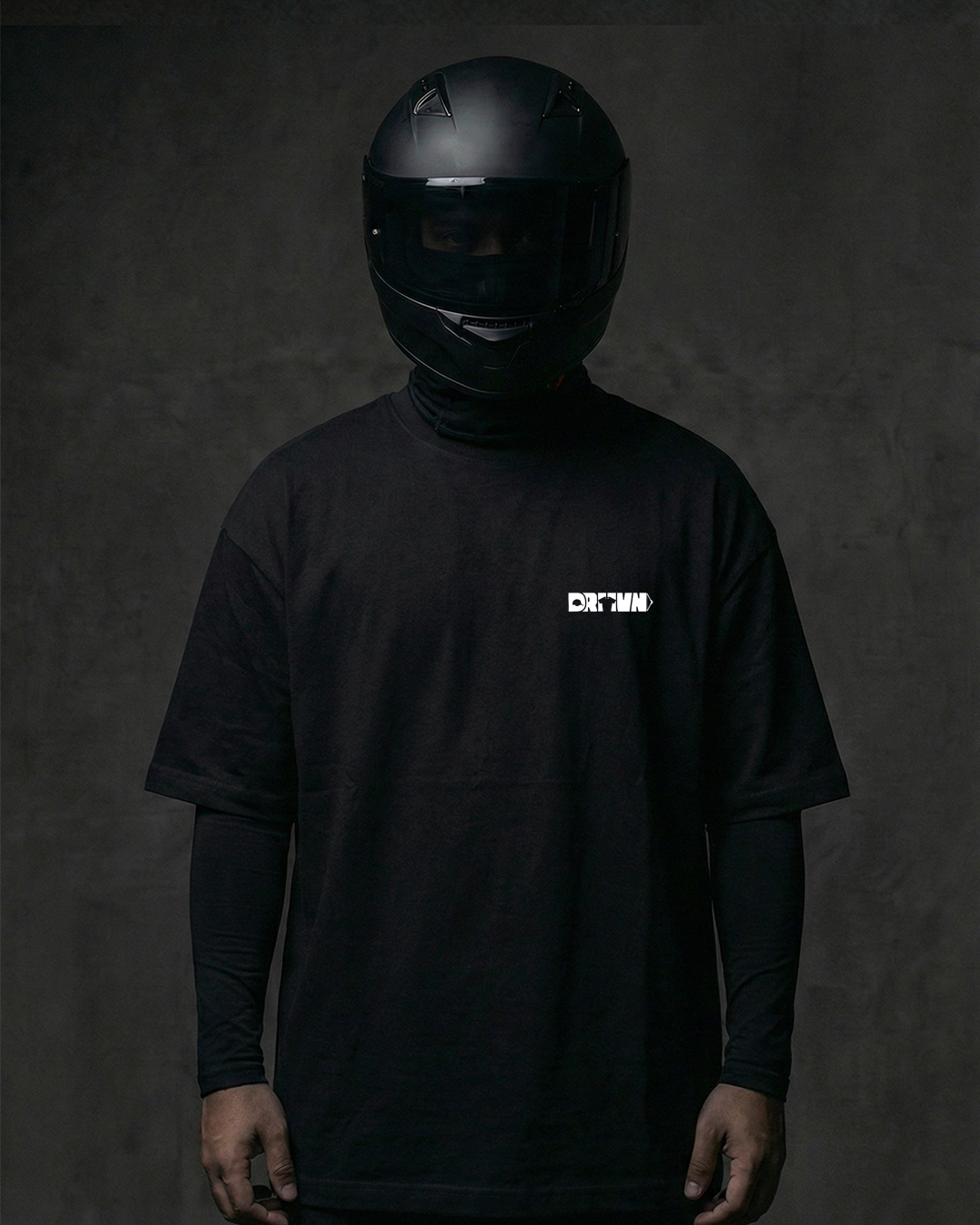 Person wearing a black helmet and black t-shirt with drivnwear logo on a dark background