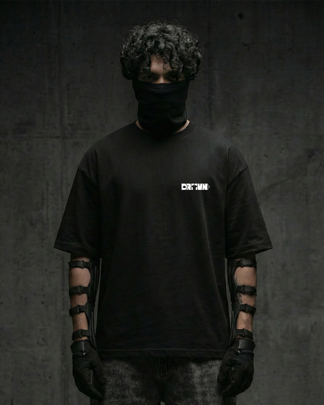 Person wearing a black t-shirt with drivn logo, black gloves, and a black balaclava against a dark background