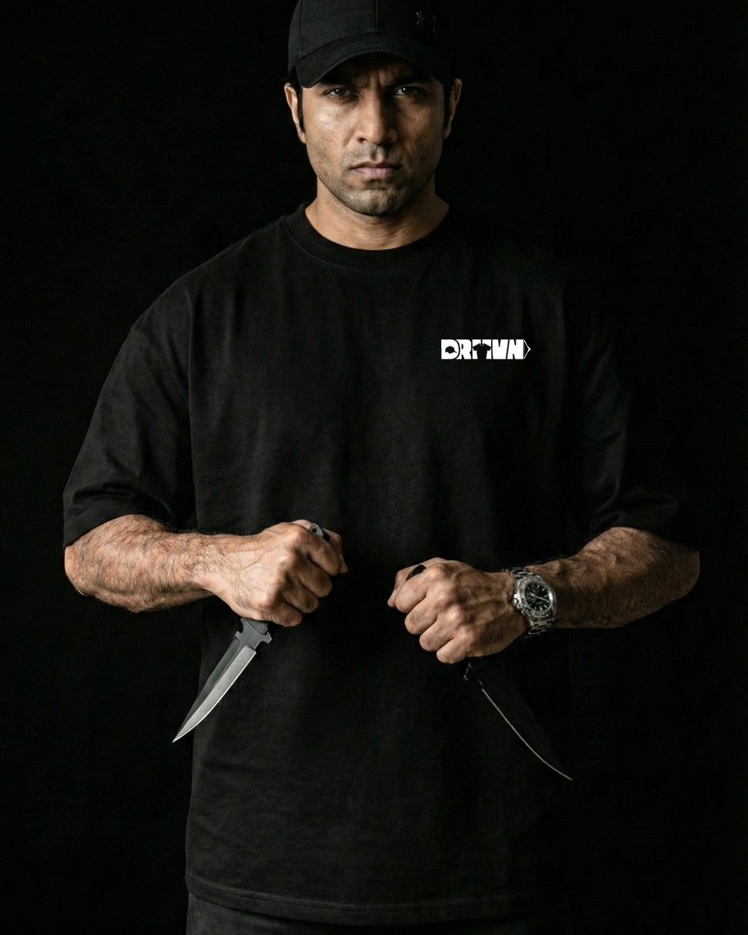 Man wearing a black t-shirt with drivnwear logo, holding a knife against a dark background