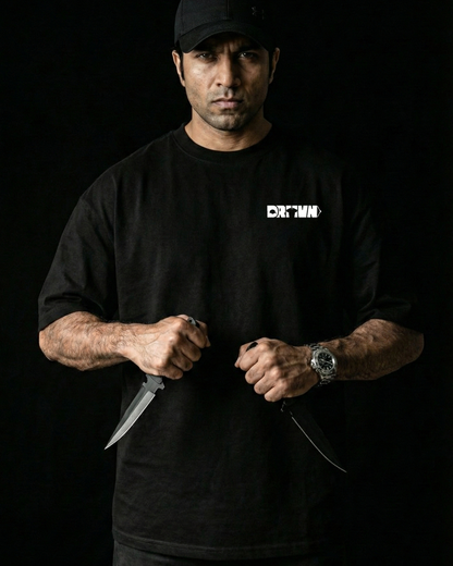 Man wearing a black t-shirt with drivnwear logo, holding a knife against a dark background